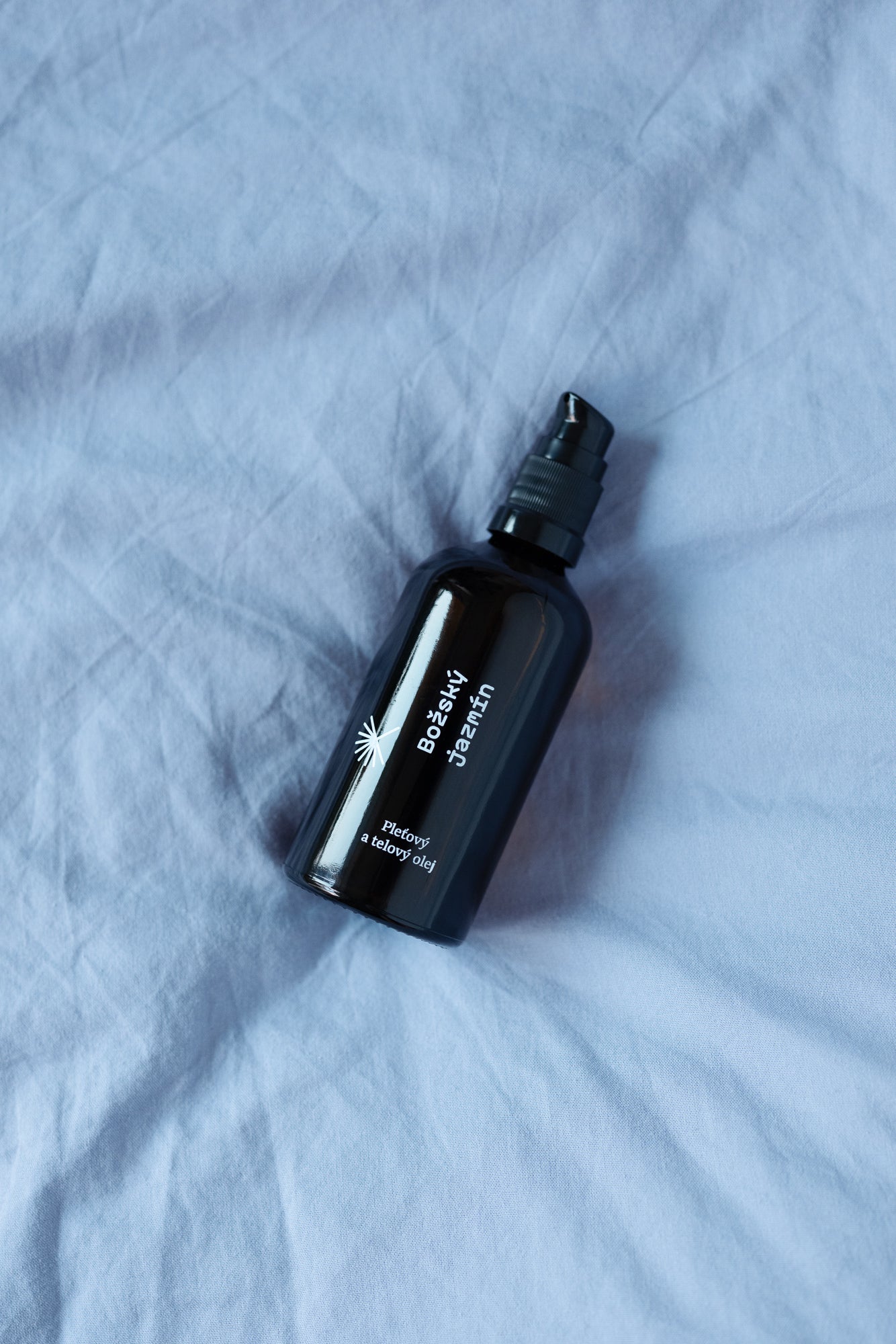 Pleťový a telový olej Božský jazmín Modrá púpava na svetlej textílii, detail sklenenej fľaštičky s pumpičkou